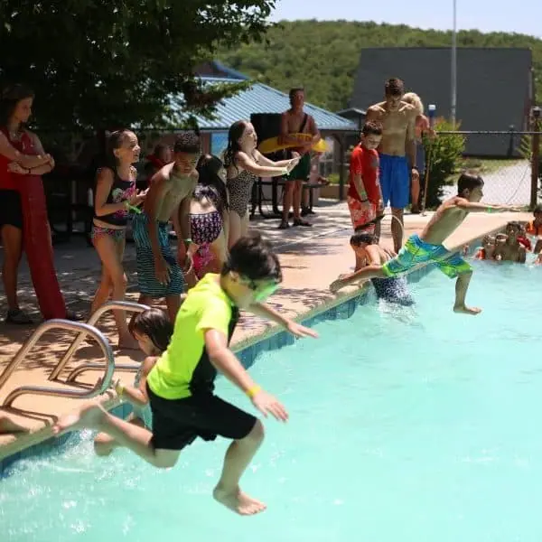 Children jumping into pool on sunny day.