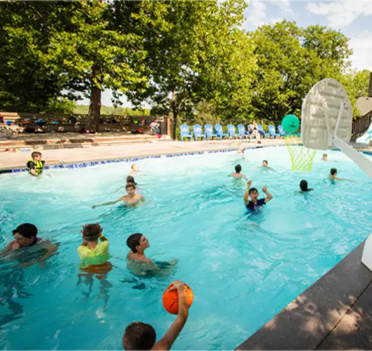 Children playing basketball in pool on sunny day.