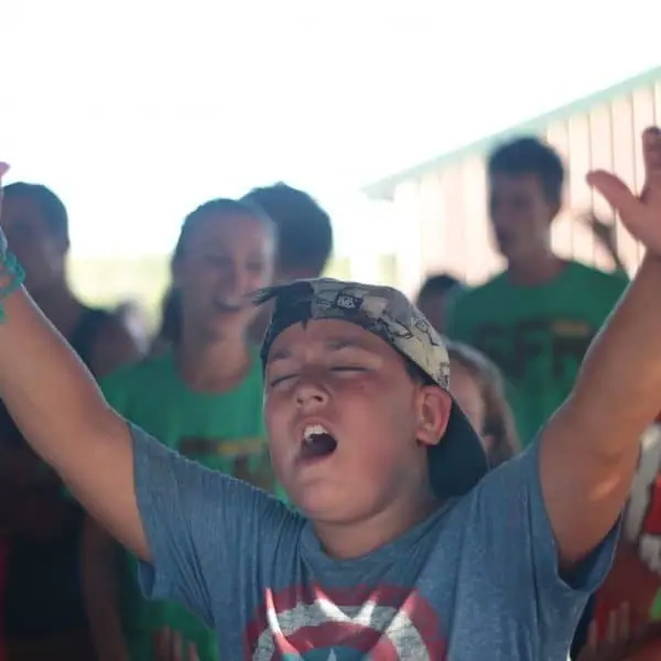 Child worshiping outdoors, hands raised.