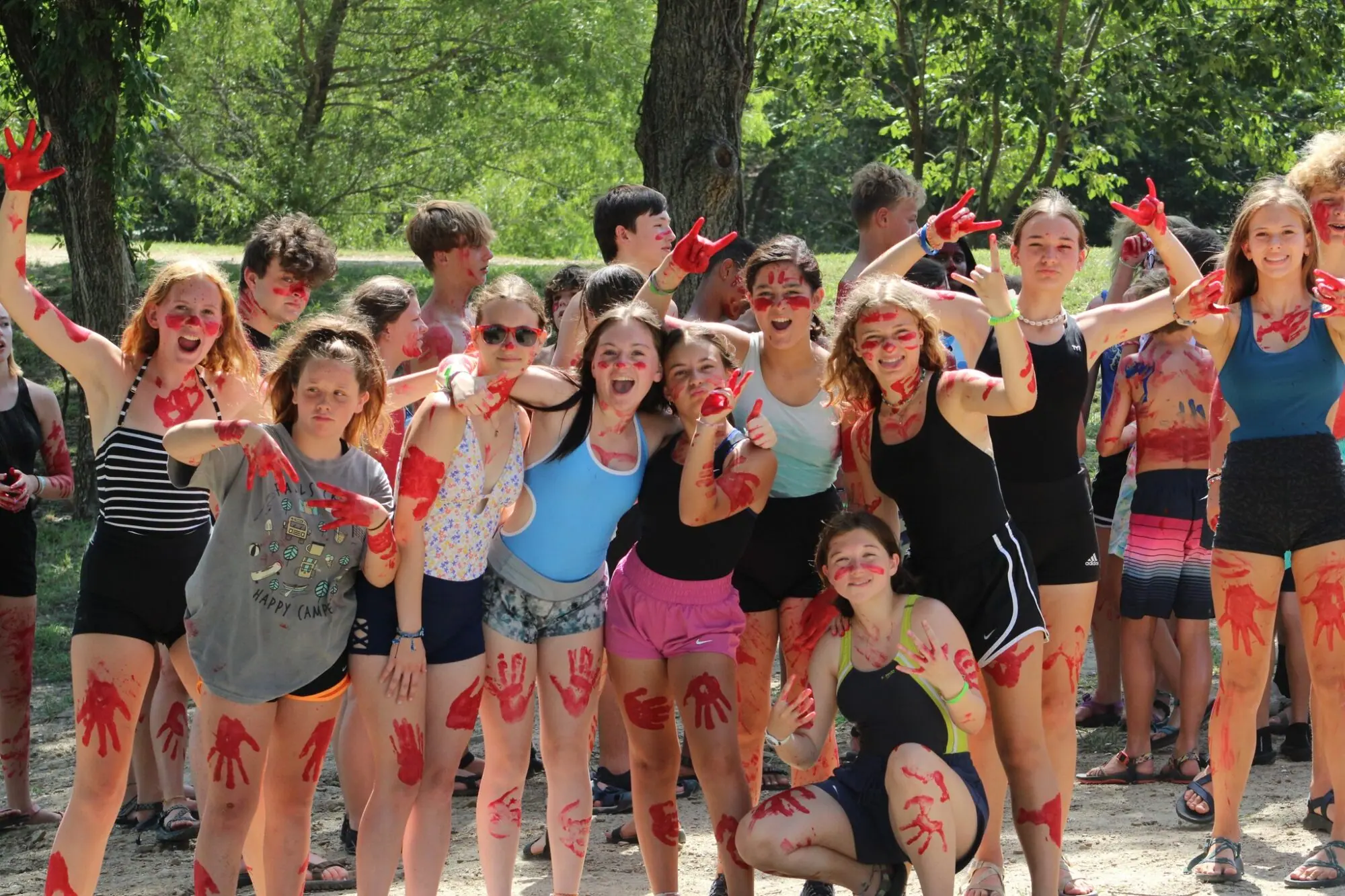 Group of teens with red face paint, smiling outdoors.