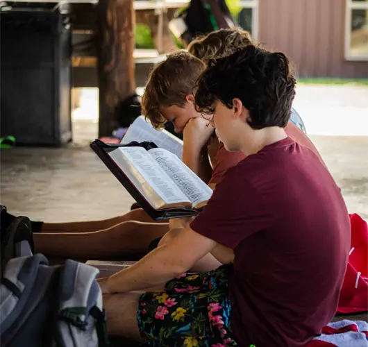 Children reading scripture outdoors together at camp