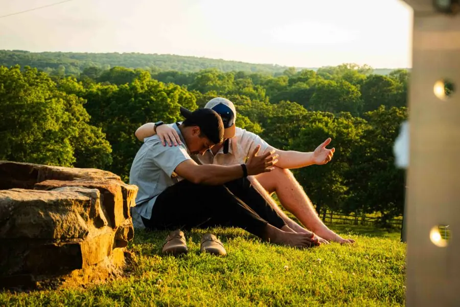 Two people praying on grassy hill at sunset.