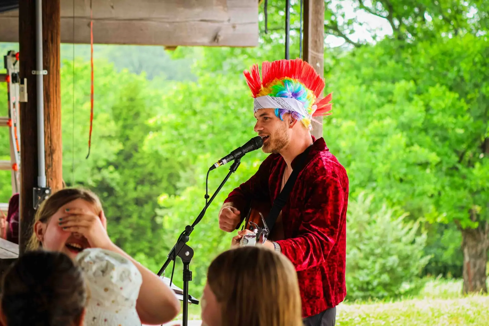 Man in colorful wig sings outdoors.
