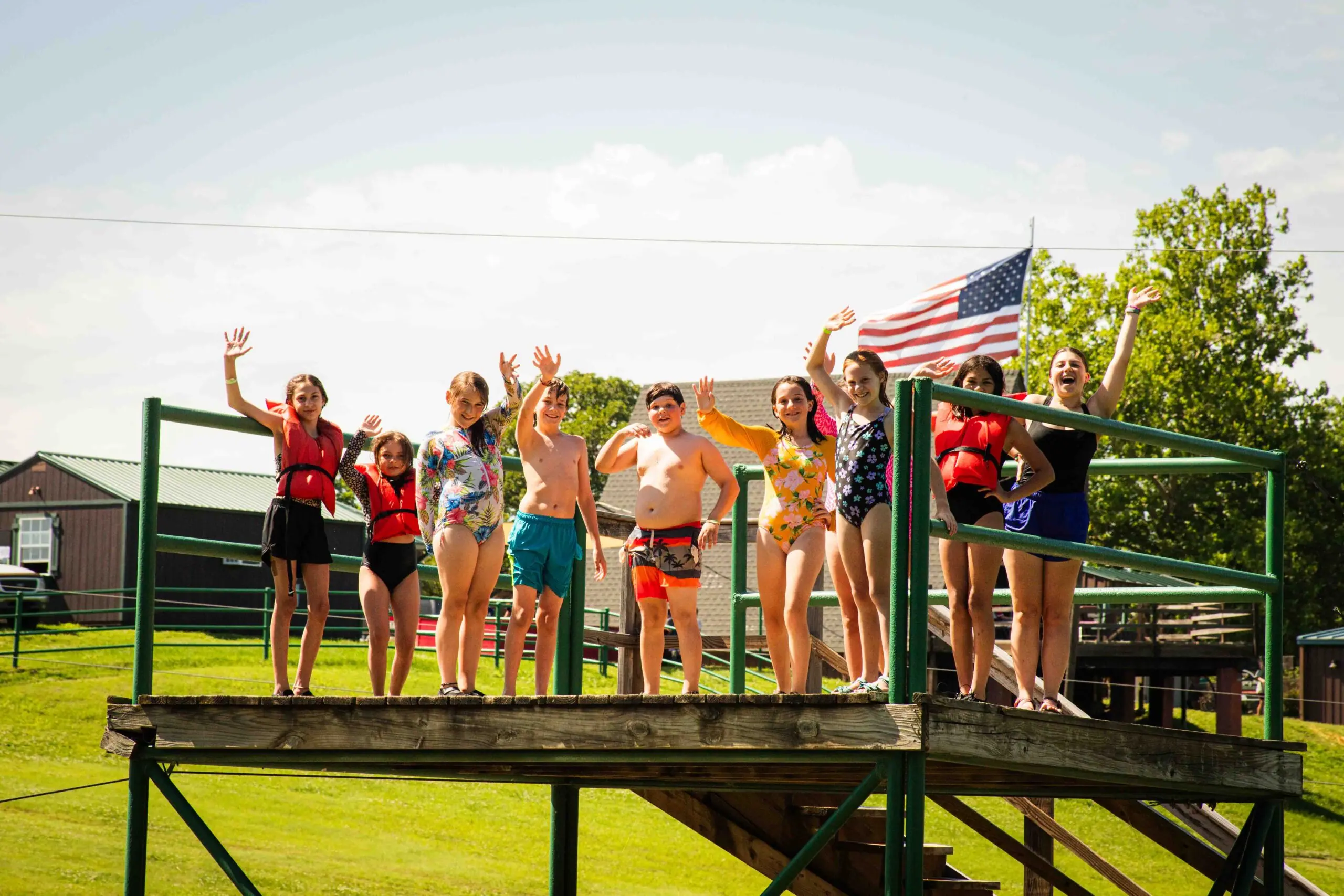 Kids waving on wooden platform at summer camp