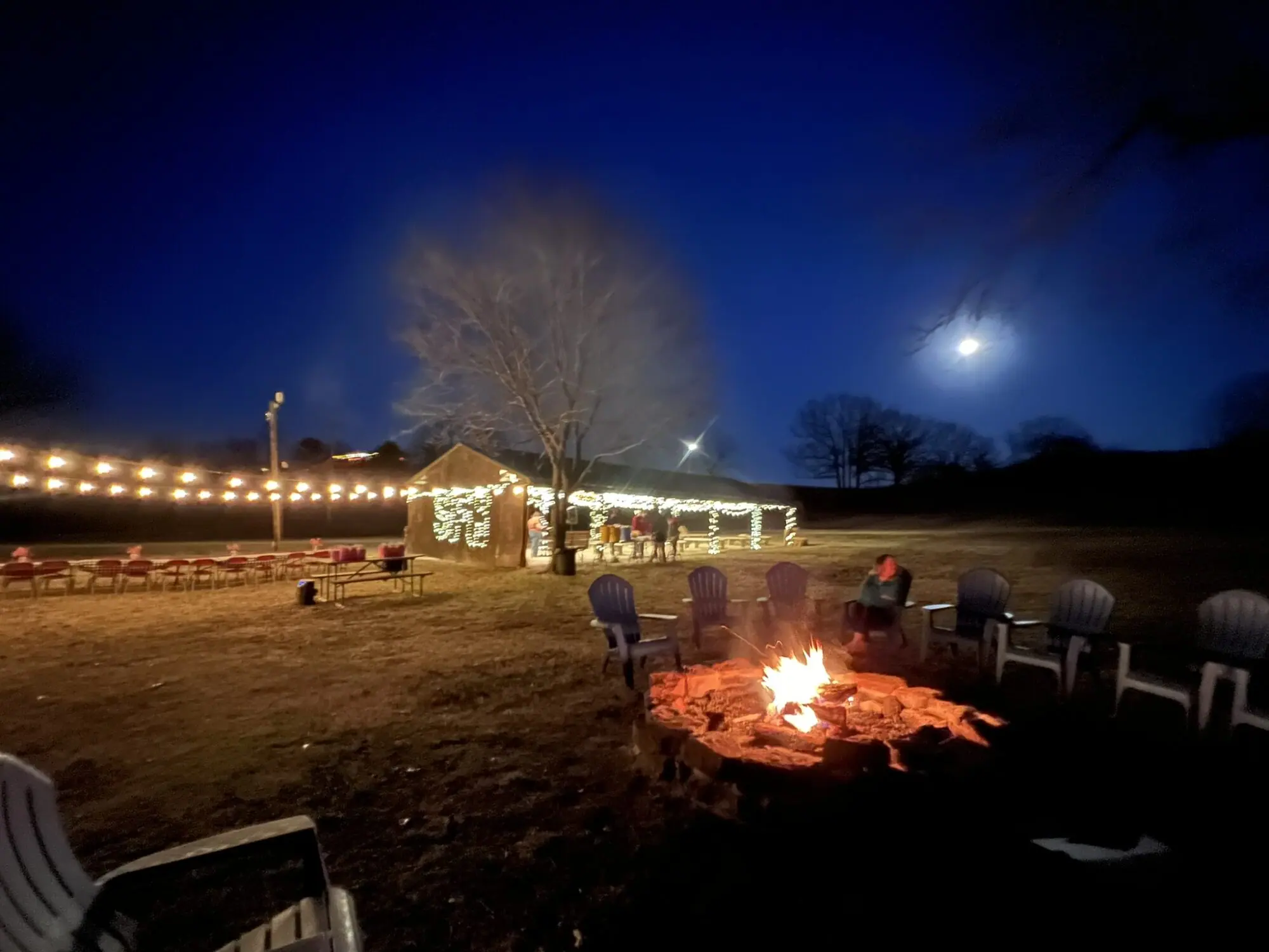 Outdoor night scene with fire pit and lights.