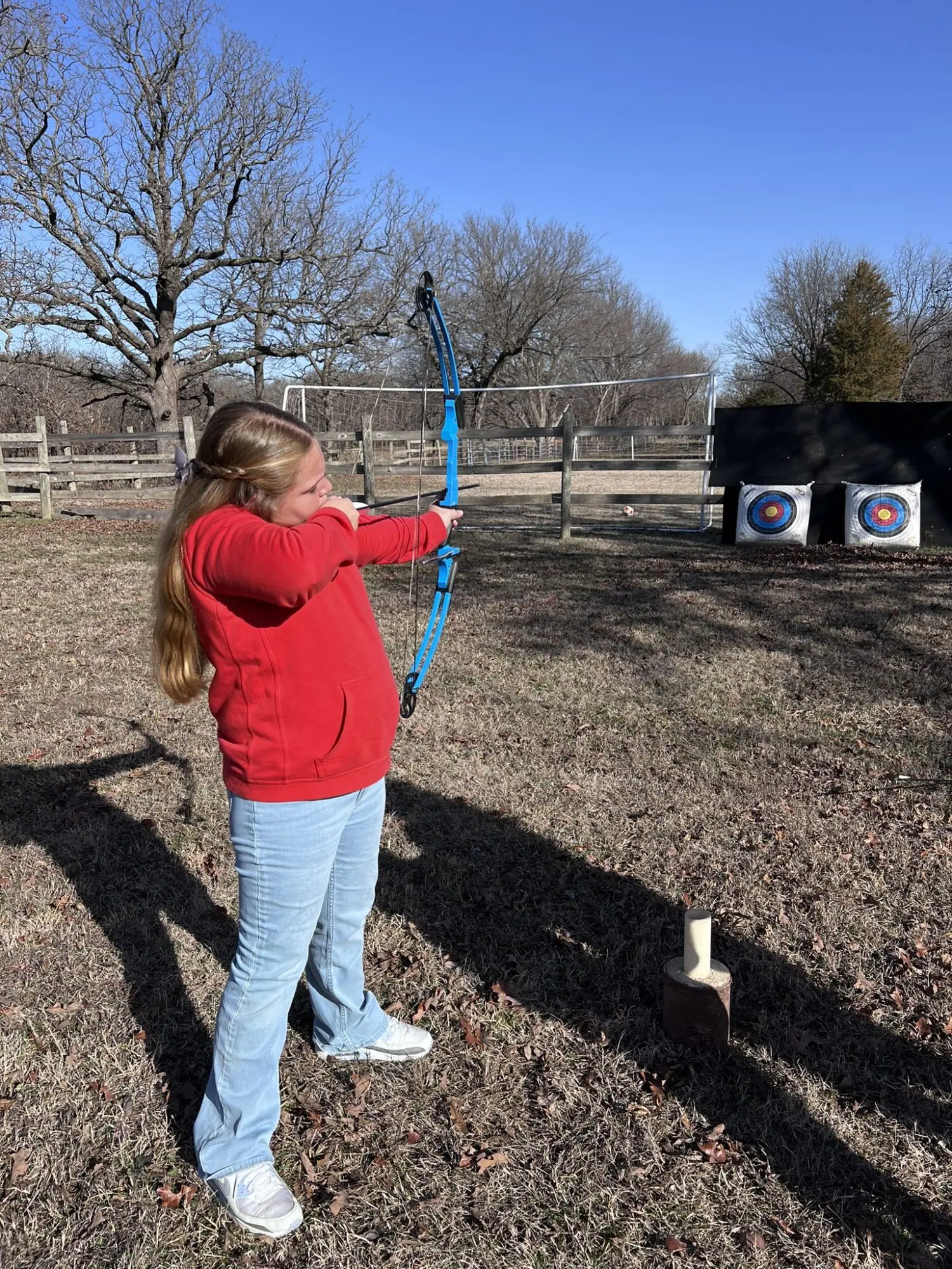 Girl practicing archery aiming at target outside.