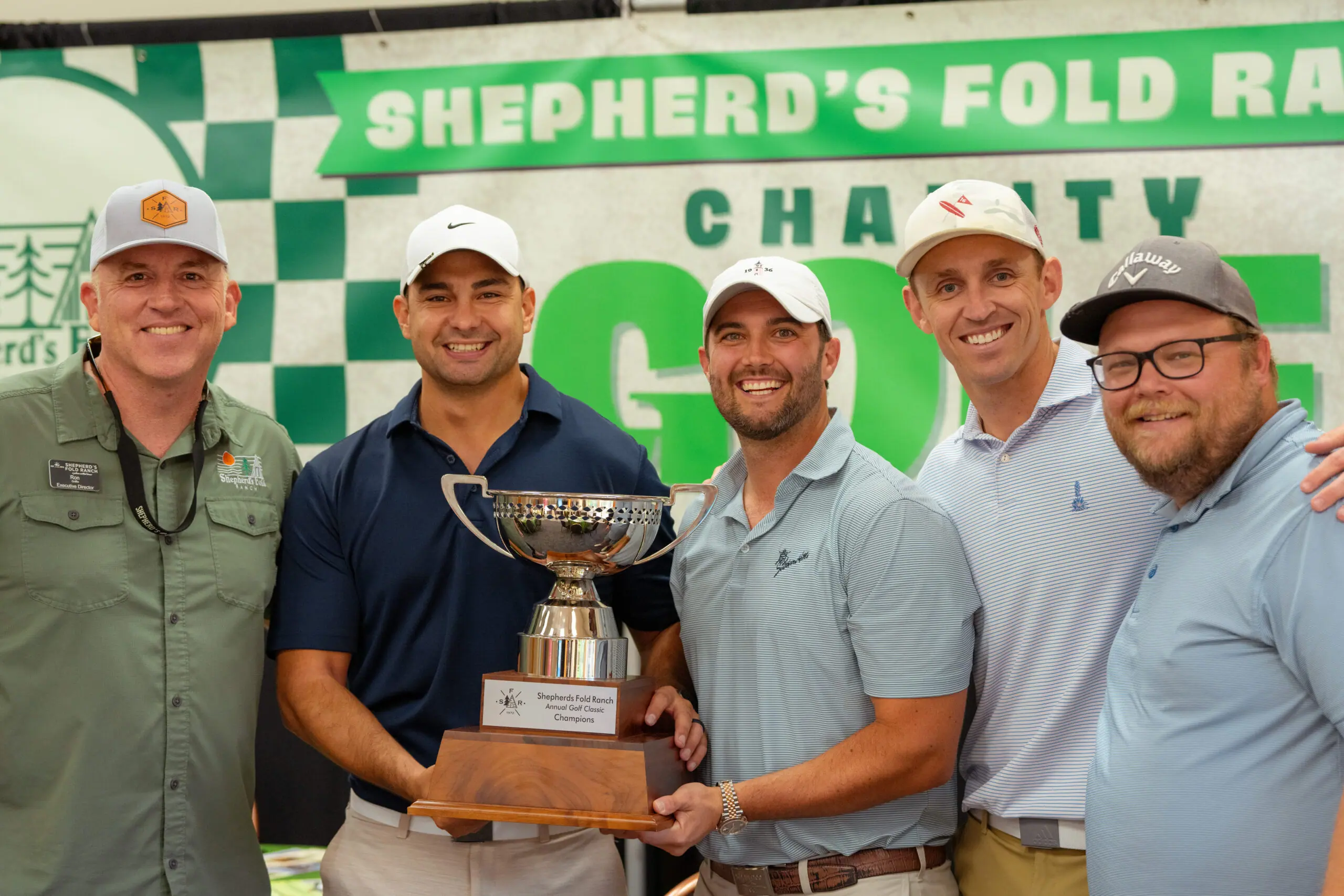 Five men holding a golf trophy, smiling.