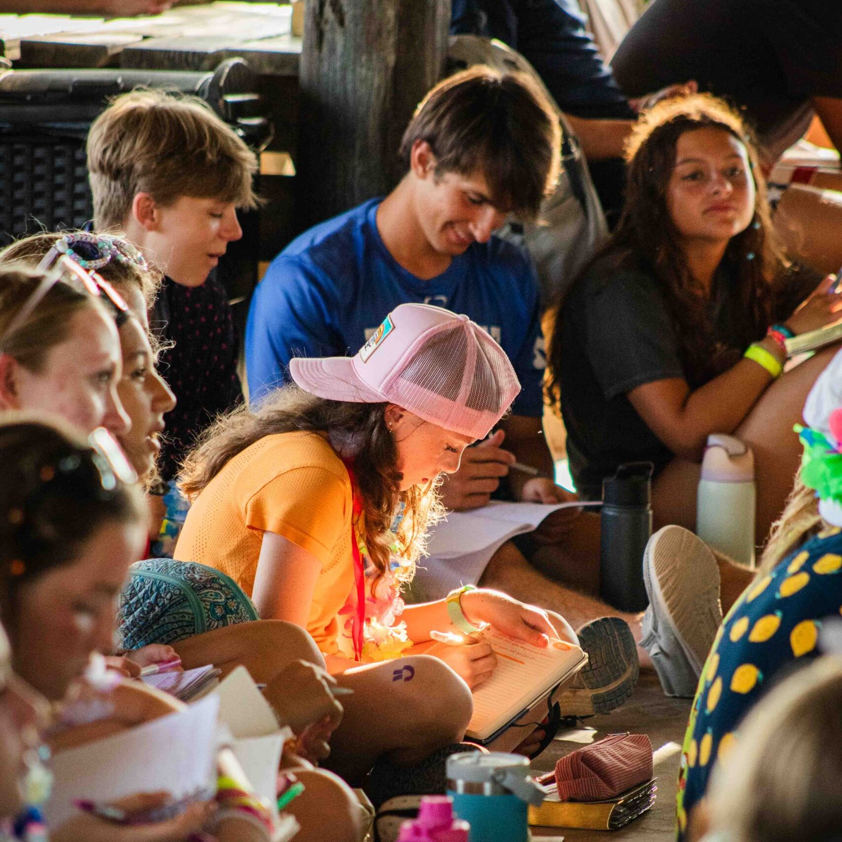 Teens writing in notebooks at summer camp.