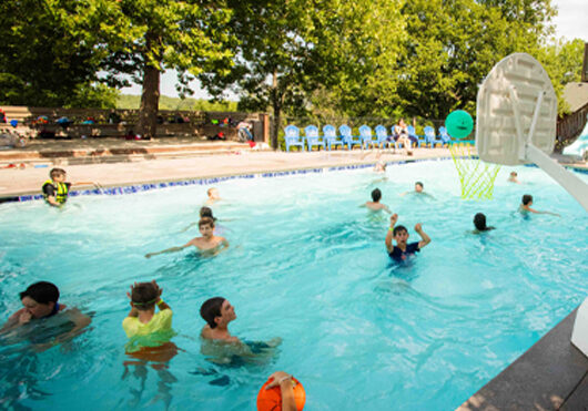 Children playing basketball in pool on sunny day.